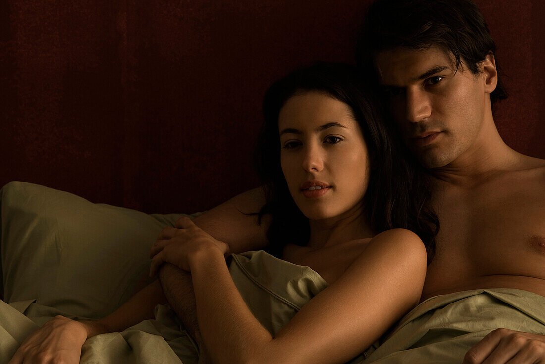 Couple reclining together in bed, man's arm around woman's shoulder
