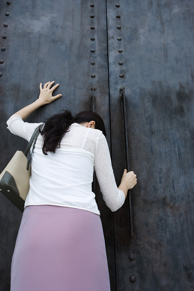 Woman standing beside closed door with head down, hand on door