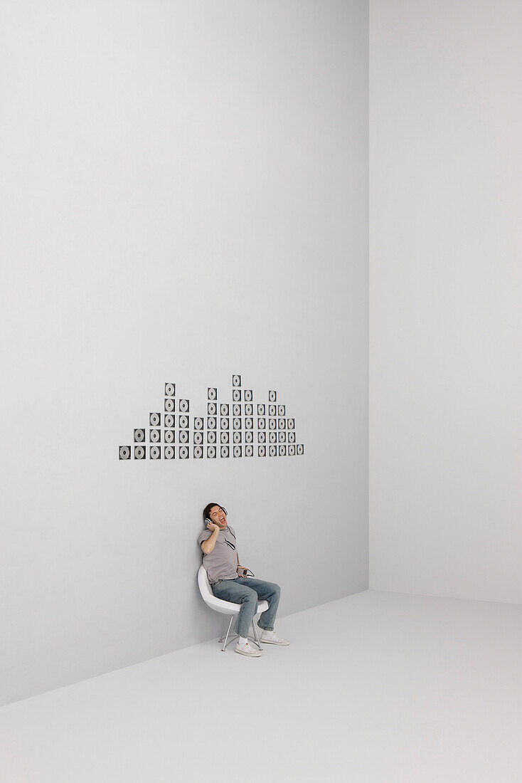 Man singing along with music playing on MP3 player, CD cases arranged in pattern on wall