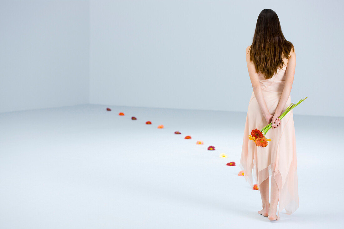 Junge Frau, die einen Blumenweg entlangläuft und einen Blumenstrauß hinter dem Rücken hält, Rückansicht