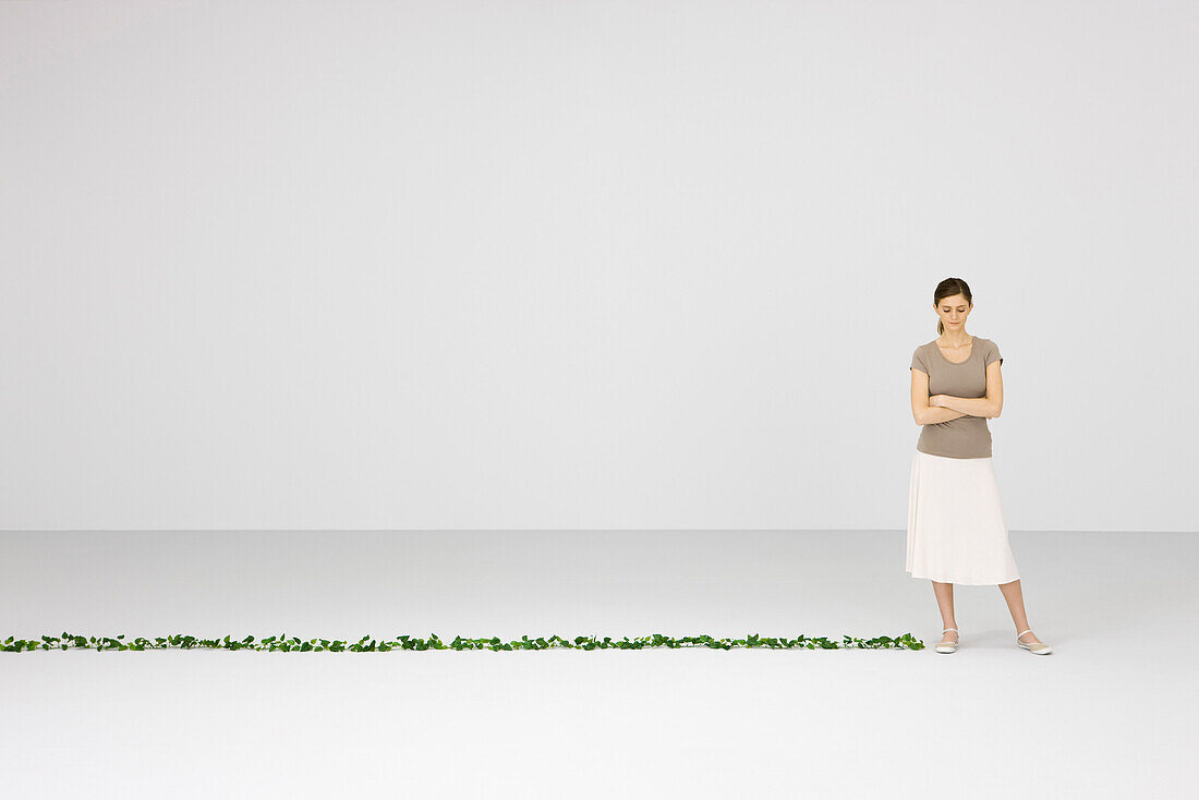 Woman standing with arms folded, looking down, vine lying on floor nearby