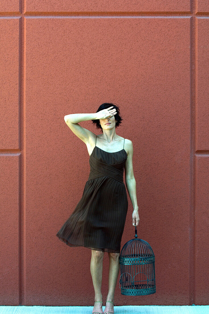 Woman holding empty birdcage, back of hand held to forehead