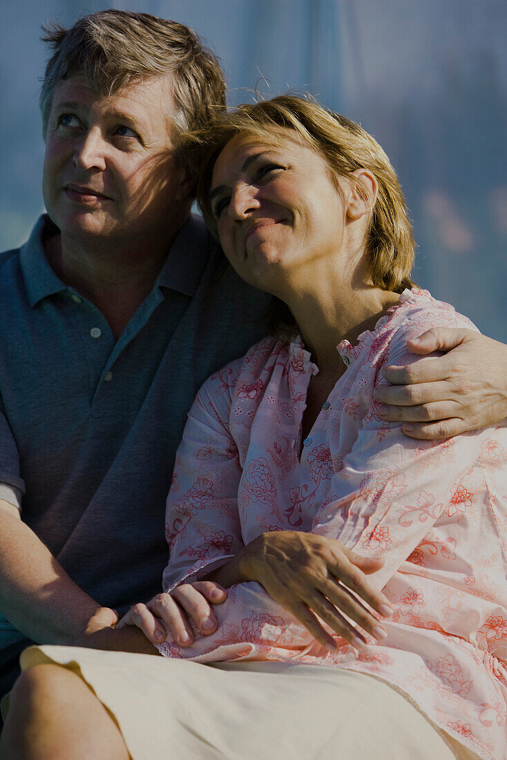 Mature couple sitting together outdoors, man's arm around woman's shoulder