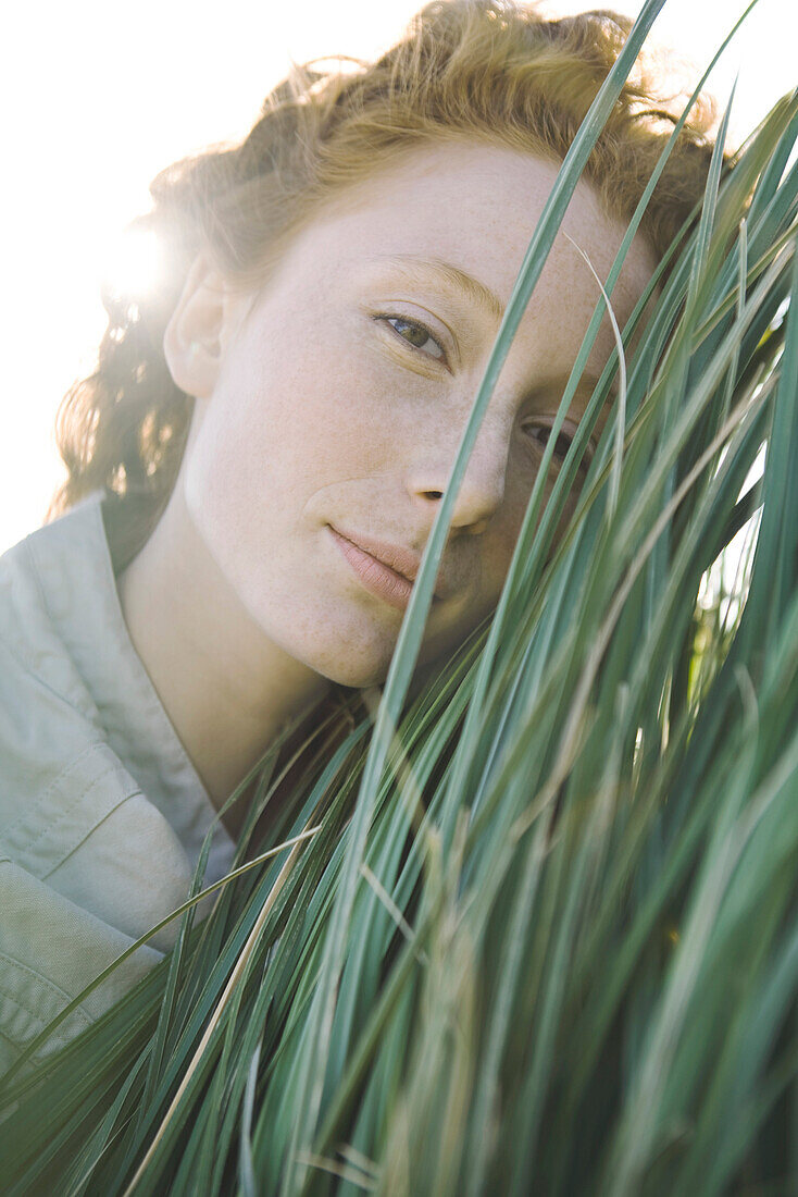 Woman with face pressed against tall grass looking at camera