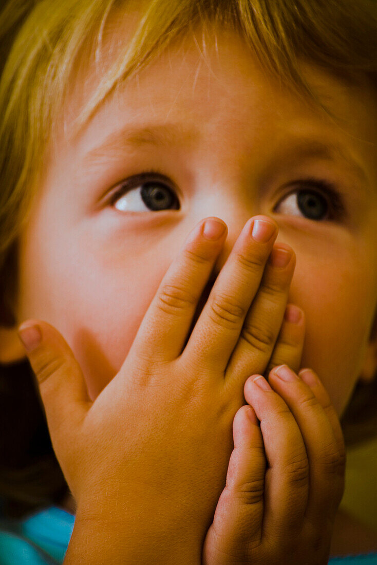 Child covering mouth with hands looking up expectantly