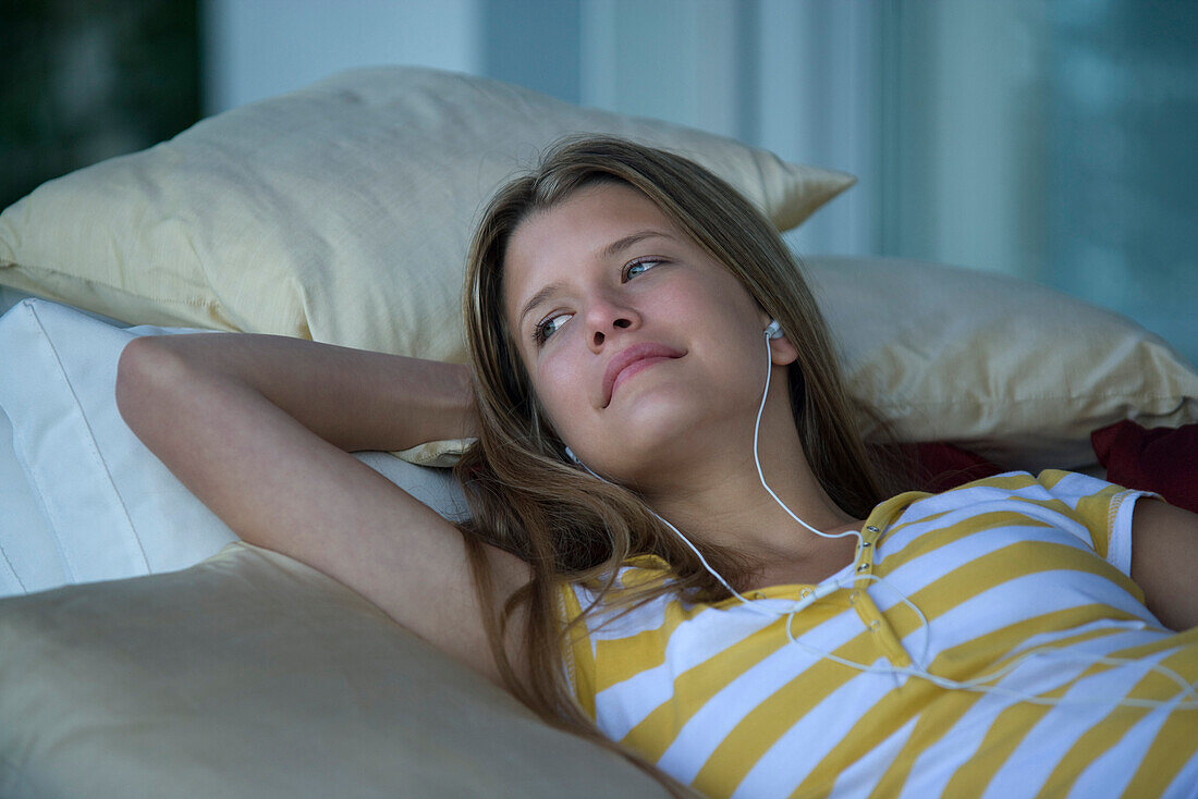 Young woman reclining on sofa, listening to earphones