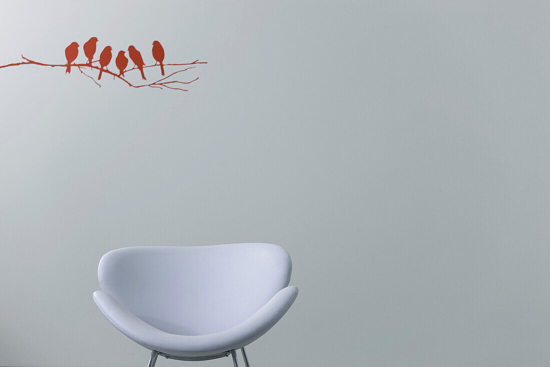 White modern chair, birds and tree branch painted on wall in background