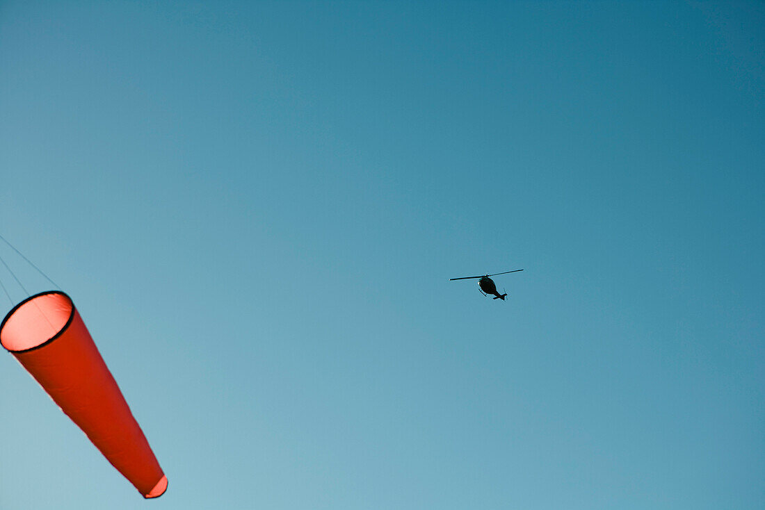 Helicopter flying above windsock in sky, low angle view