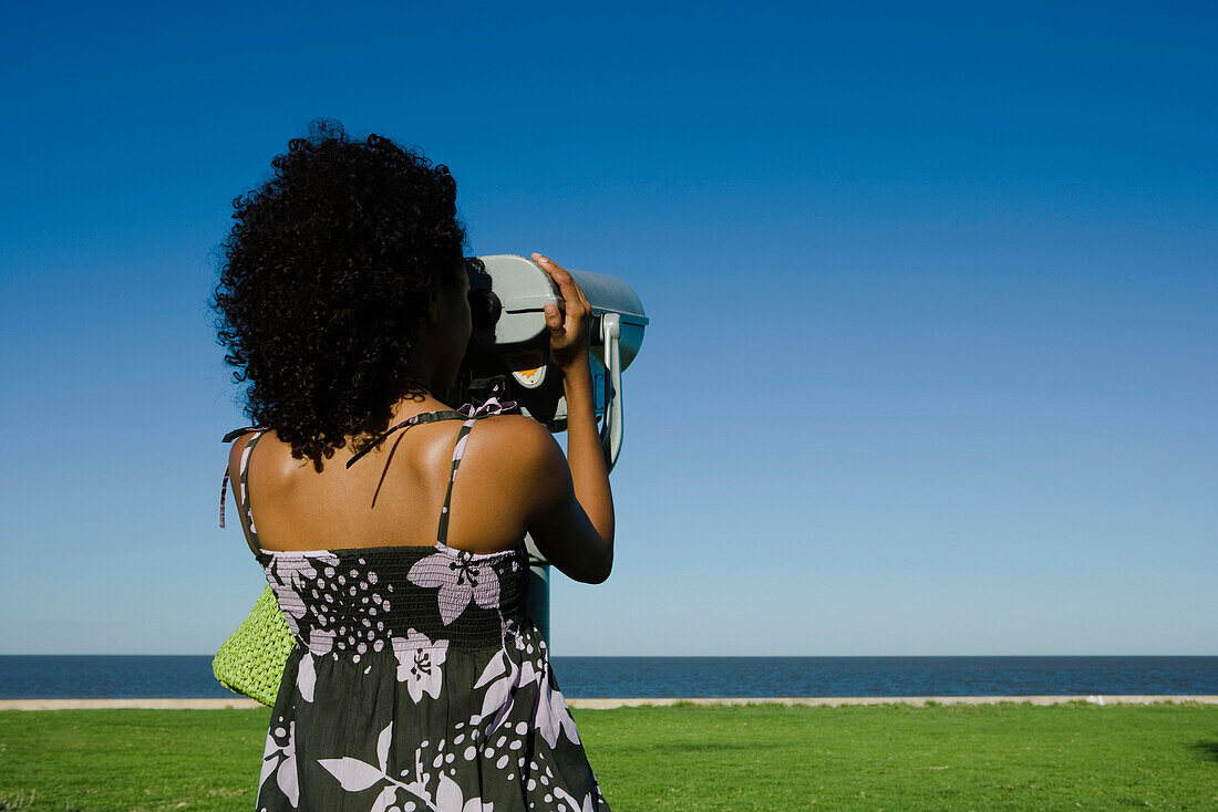 Young woman looking at sea through pay binoculars