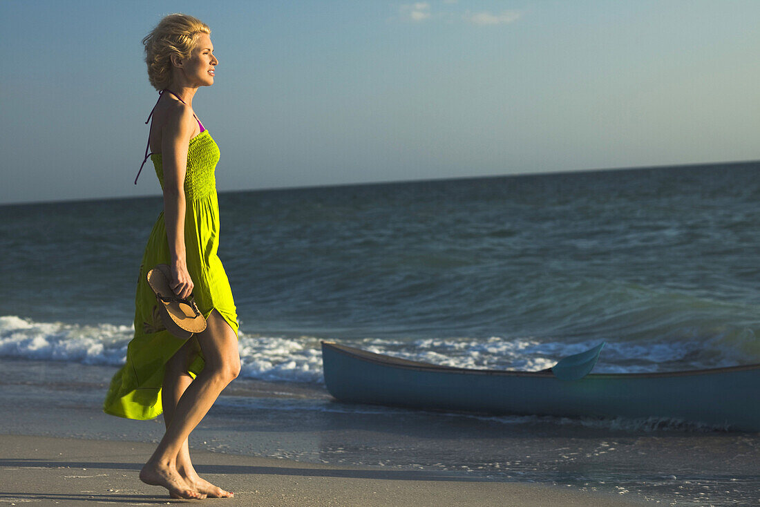 Woman in sundress walking on beach, looking at sea