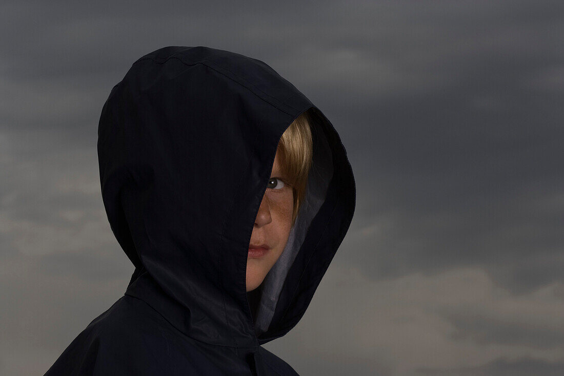 Boy with face partially obscured by jacket hood, looking at camera