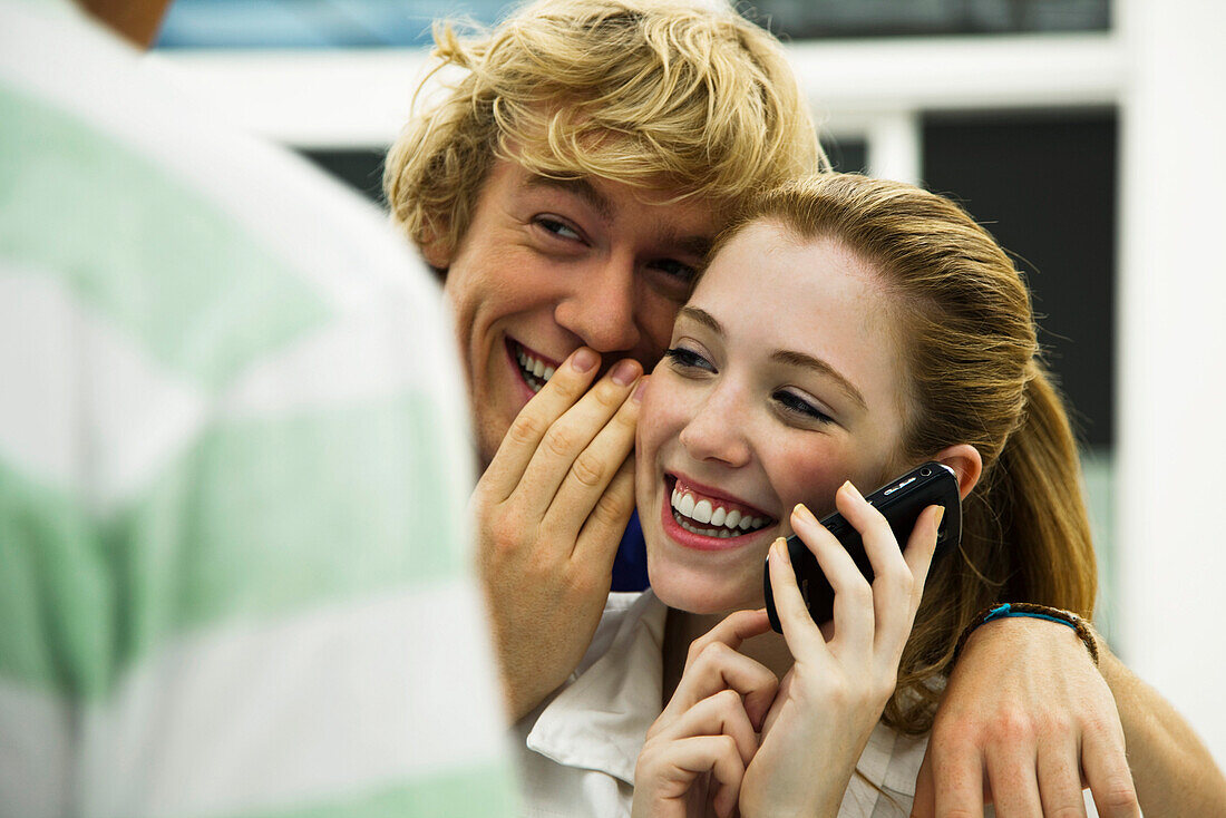 Young friends gossiping while one listens to cell phone