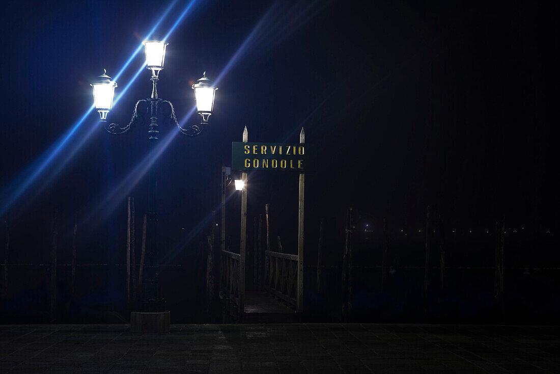 Italy, Venice, illuminated street lamp and gondola stand along the Grand Canal at night