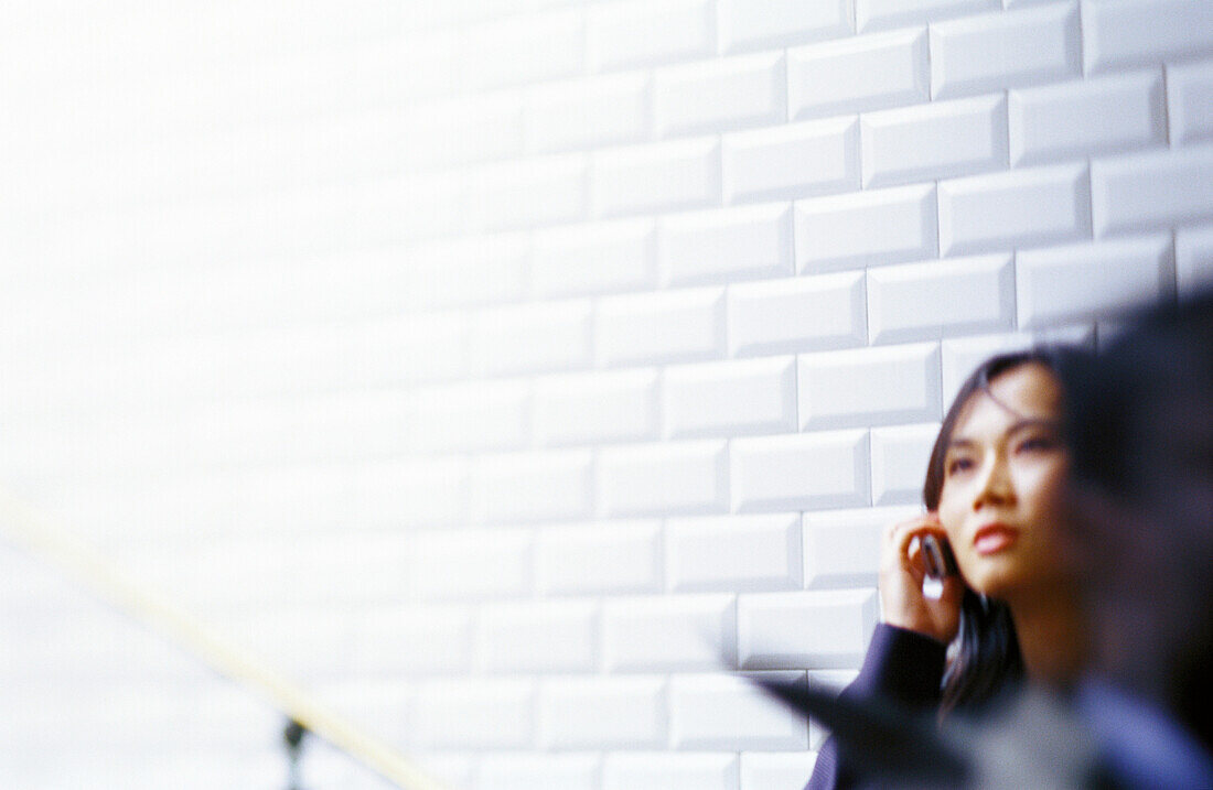 Woman talking on cell phone leaning against tiled wall
