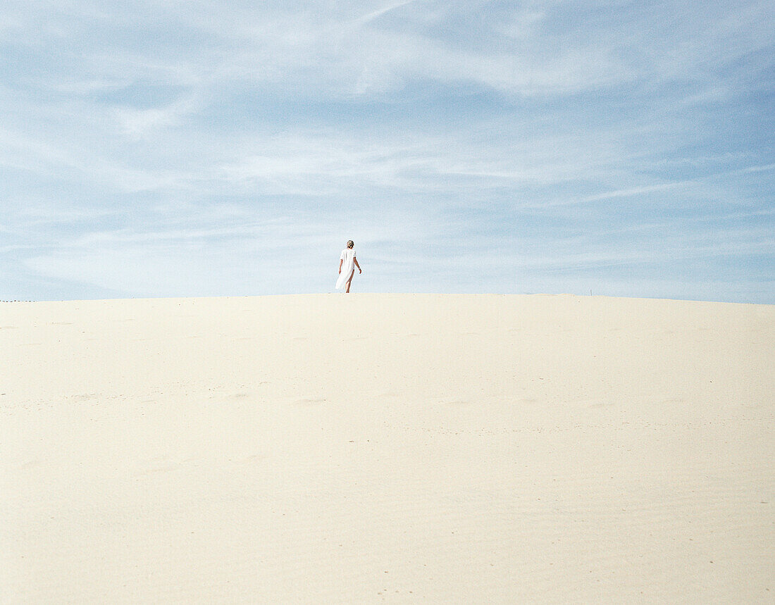 Woman standing on sand, in distance