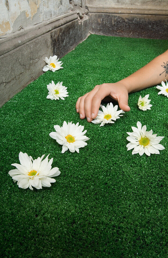 Woman picking up flower from artificial turf, cropped view of arm