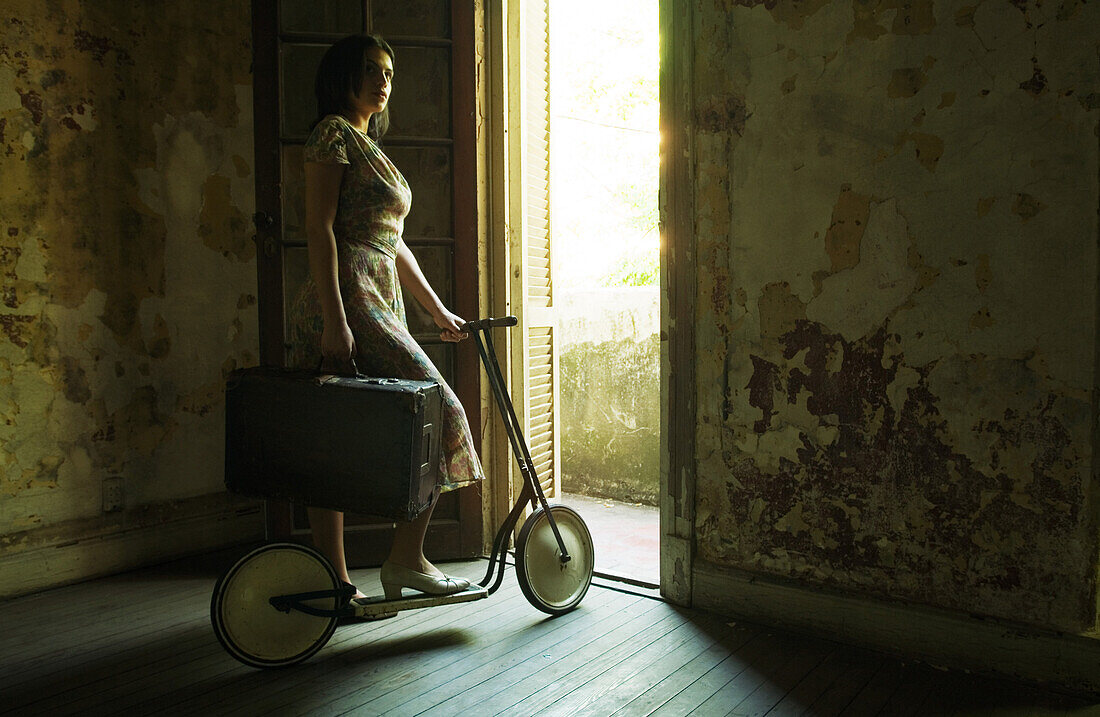 Woman standing by doorway on scooter, holding suitcase