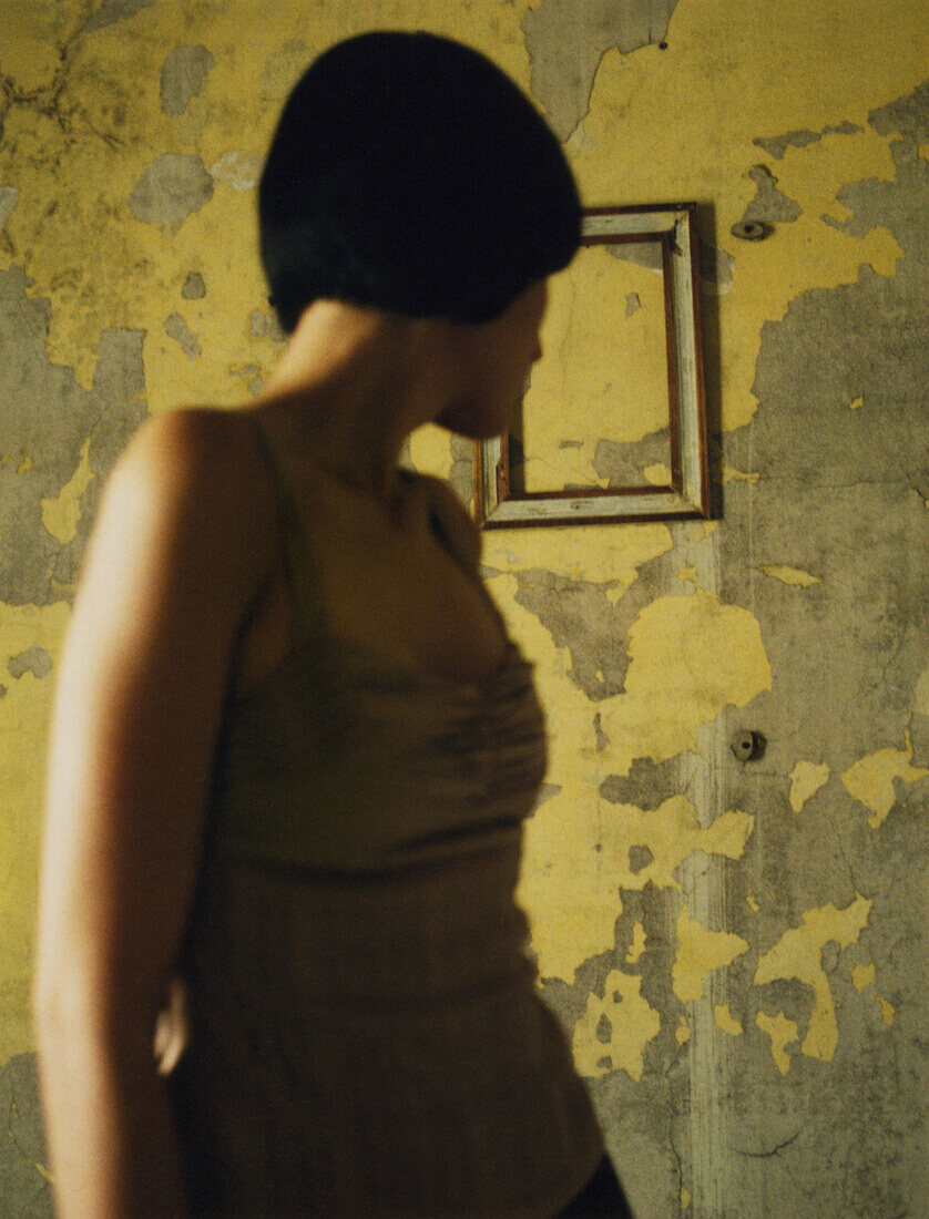 Woman looking over shoulder at frame on flaking wall, focus on background