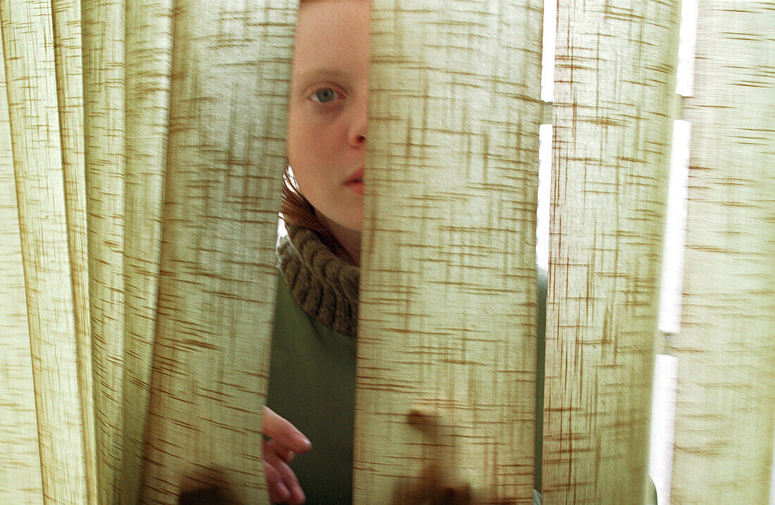 Young woman standing behind curtain