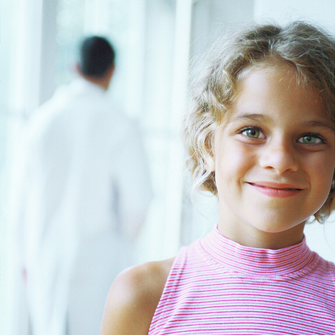 Girl smiling, doctor walking away in background