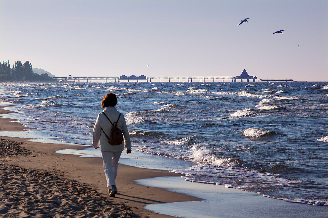 Woman walking along the beach towards the pier, Heringsdorf seaside resort, Usedom island, Baltic Sea, Mecklenburg-West Pomerania, Germany