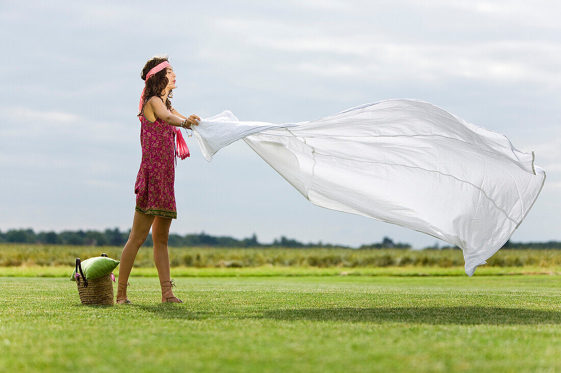 Young woman setting a sheet on the grass, oudoors