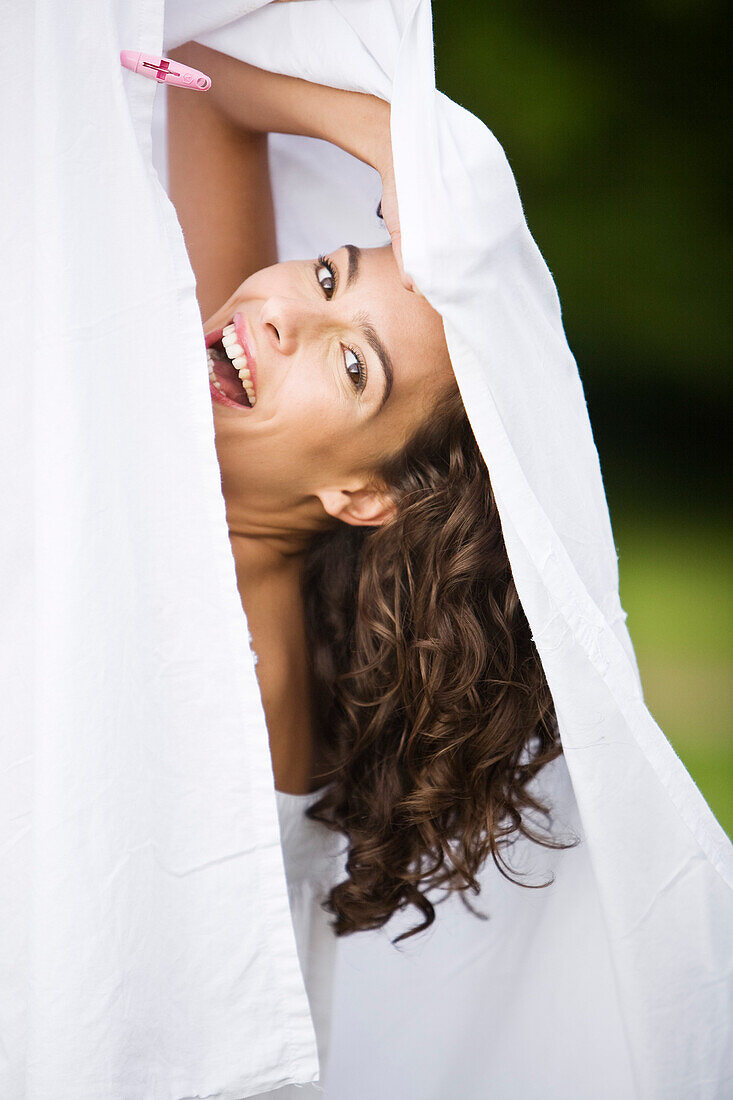 Young woman laughing, behind a white sheet, oudoors