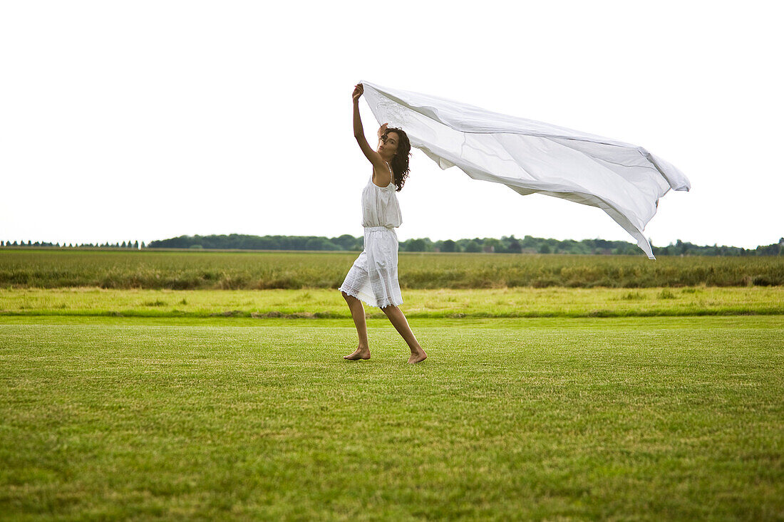 Young woman walking and holding a white sheet, oudoors