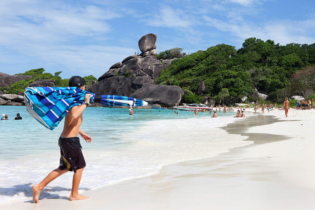 Junge bringt Sonnenschirm an den feinem weissen Sandstrand am Sail Rock, Similan Inseln, Andamanensee, Thailand