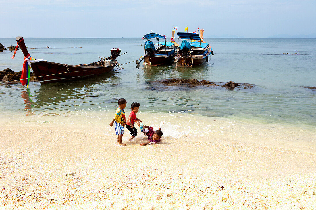 Thailändische Kinder spielen am Strand bei Longtailbooten, Koh Jum, Andamanensee, Thailand