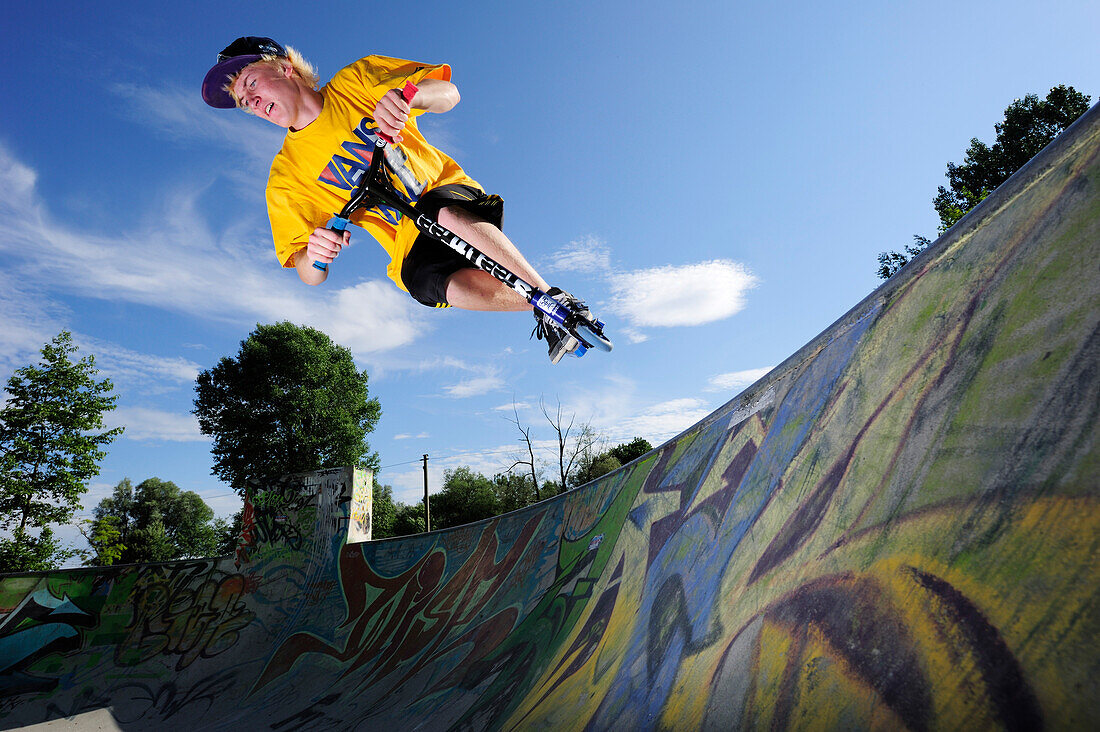 Junger Mann im Sprung mit einem Tretroller, Skatepark, München, Oberbayern, Bayern, Deutschland