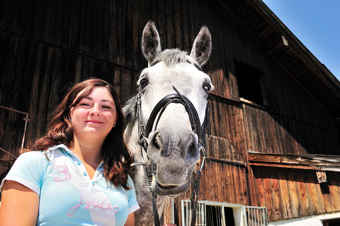 Porträt einer Frau mit einem Pferd vor einem Pferdestall, Inntal, Oberbayern, Bayern, Deutschland