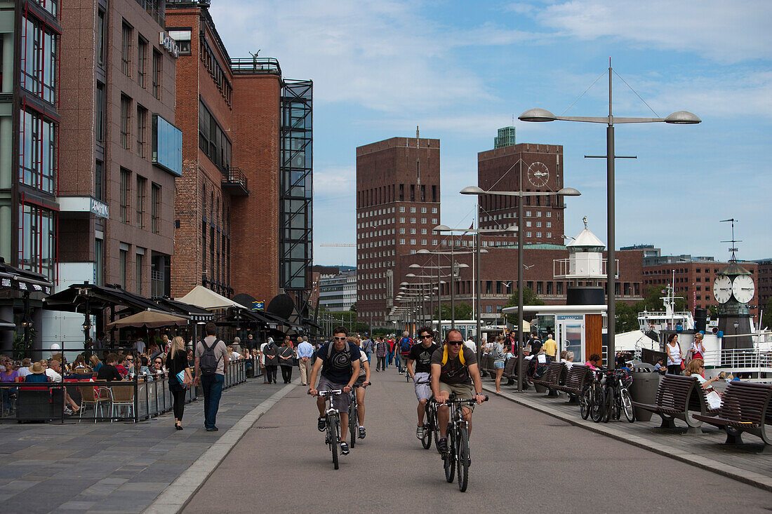 Radfahrer an der Hafenpromenade mit Rathaus im Hintergrund, Oslo, Südnorwegen, Norwegen