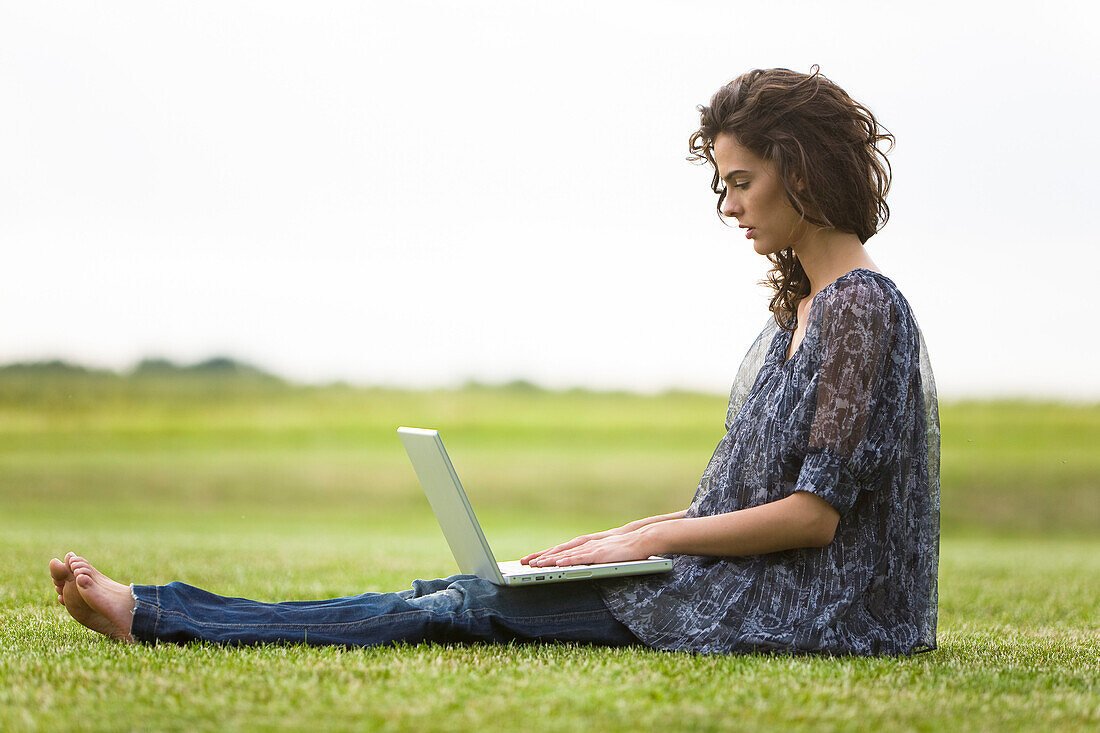 Young woman sitting in grass, using laptop computer