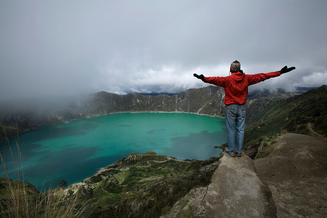 Man With Outstretched Arms Standing at Top of Large Crater Filled With Water, Quilatoa, Ecuador