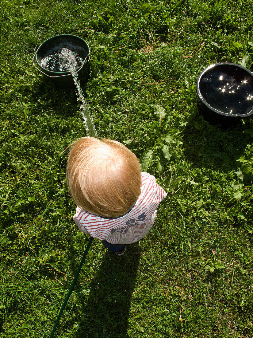 Young Blonde Boy Putting Water in Bucket With Hose