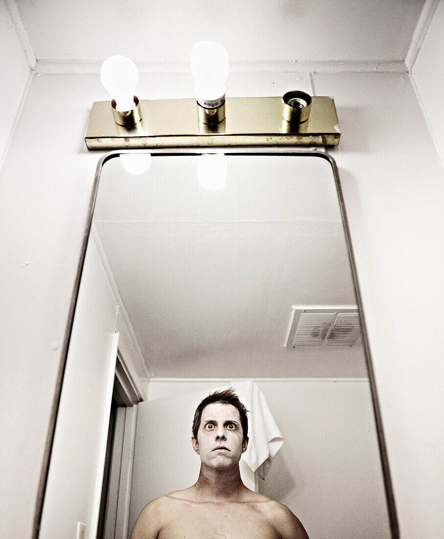 Wide-Eyed Man With White Face Mask Looking in Mirror