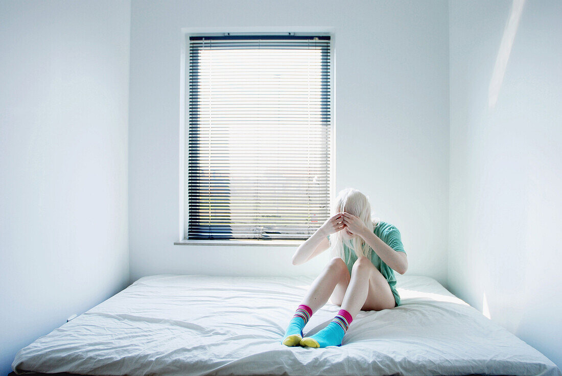 Teenage Girl With Hands and Blonde Hair Covering Face Sitting on Bed