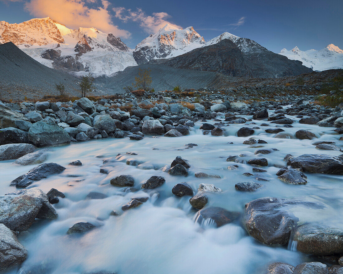 Fluss mit Steinen vor schneebedeckten Bergen in der Abendsonne, Val Roseg, Piz Bernina, Piz Roseg, Graubünden, Schweiz, Europa