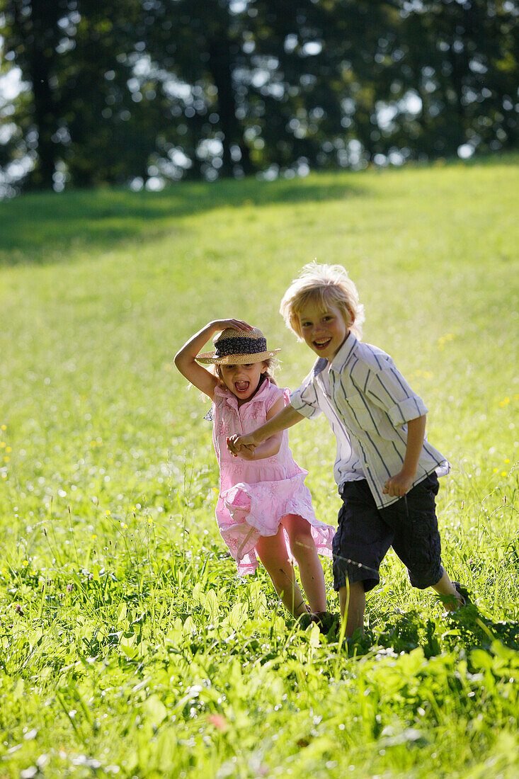 Sibling (5 and 7 years) running over a meadow, Lake Starnberg, Bavaria, Germany