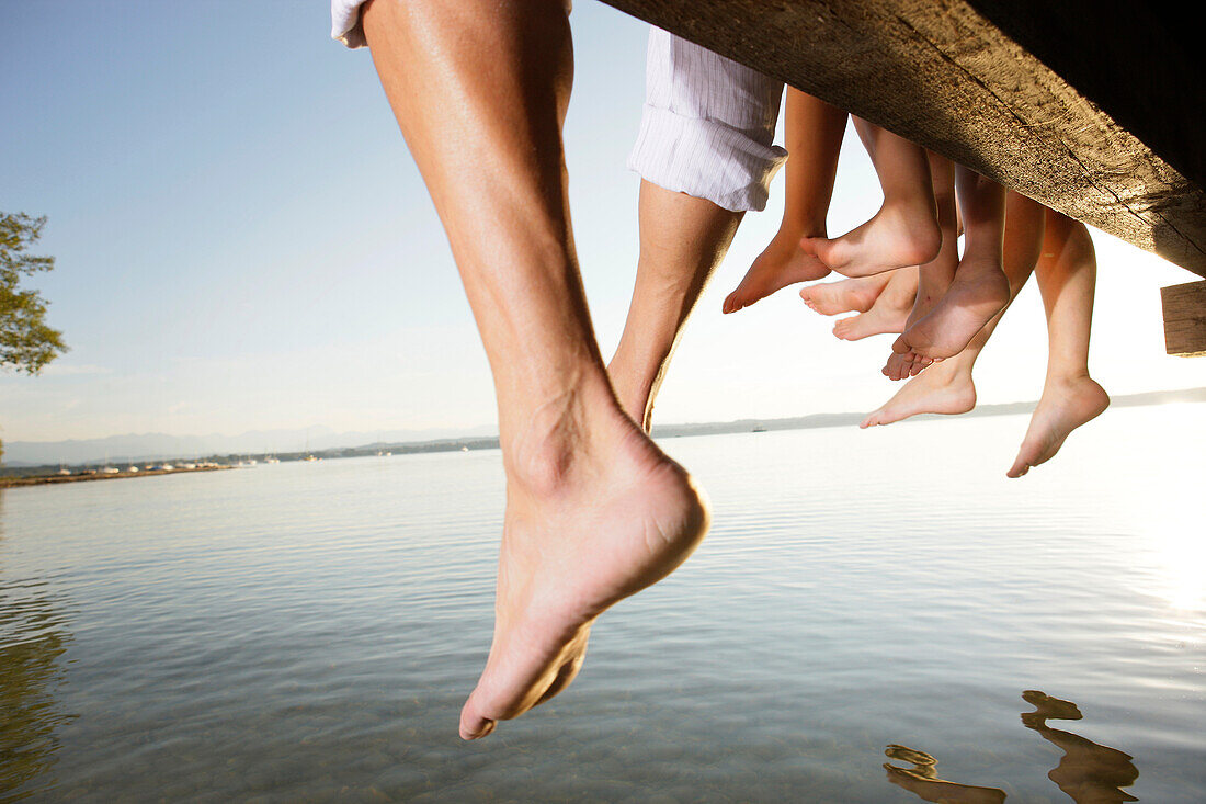 Family sitting on a jetty, close-up feet, Lake Starnberg, Bavaria, Germany