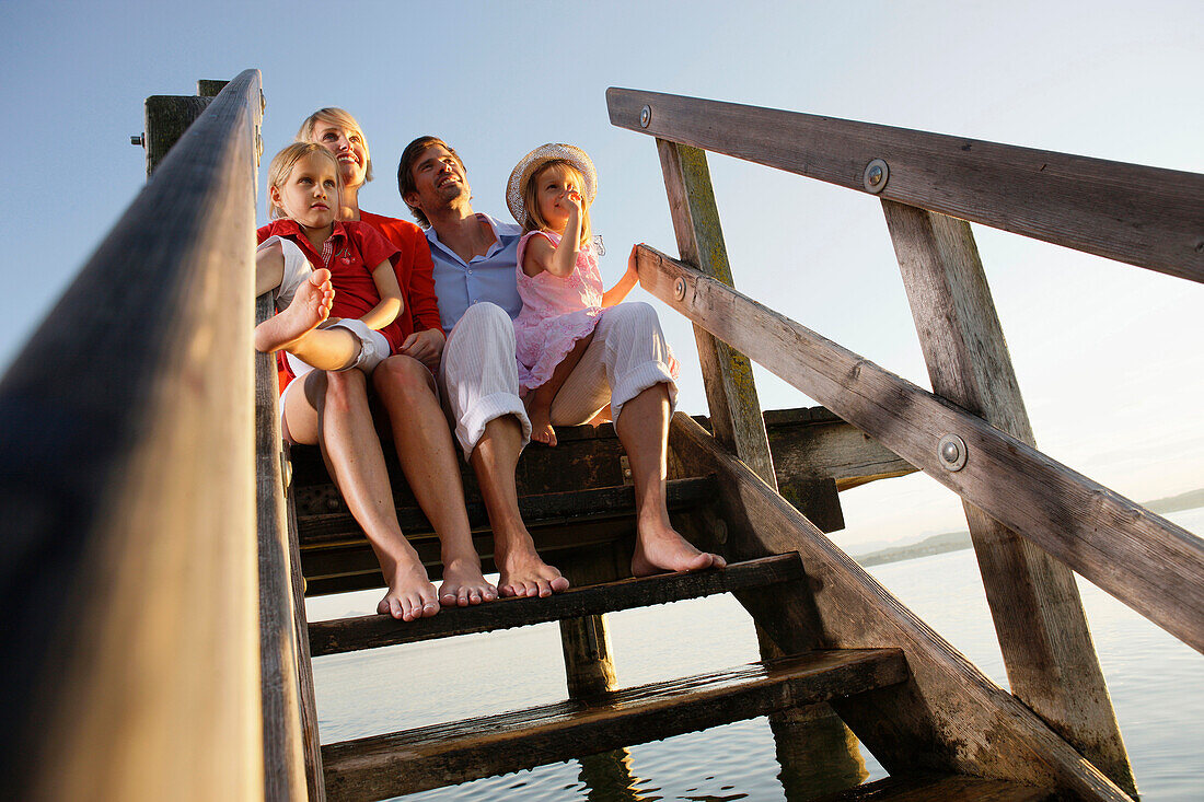 Familie sitzt auf einem Steg am Starnberger See, Bayern, Deutschland