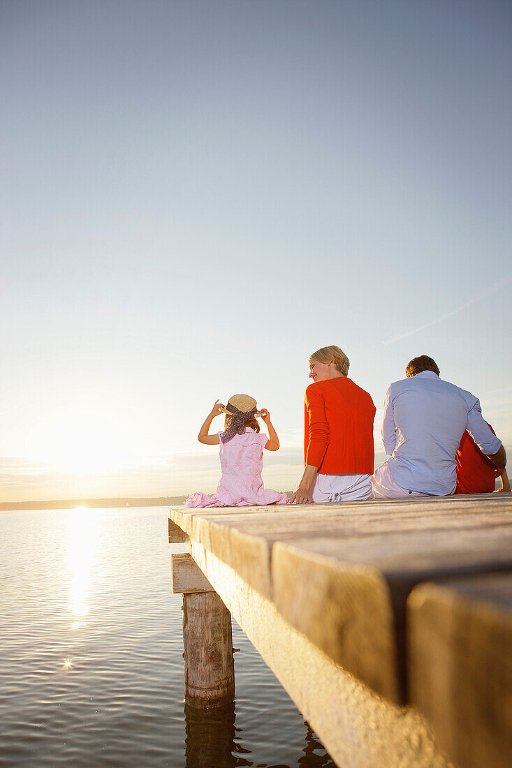 Familie sitzt auf einem Steg am Starnberger See, Bayern, Deutschland