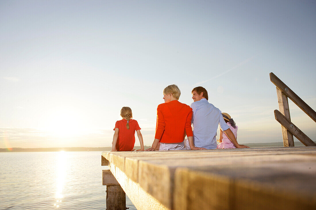 Familie sitzt auf einem Steg am Starnberger See, Bayern, Deutschland