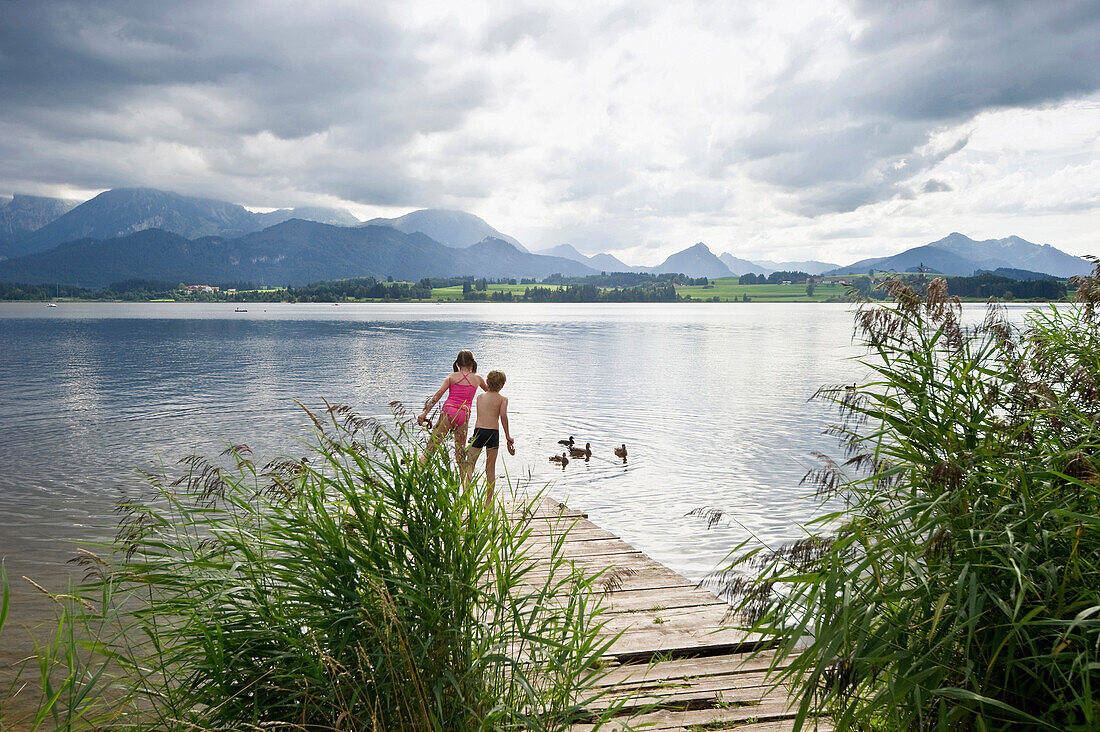 Two children on a jetty at lake Hopfensee, Fuessen, Allgaeu, Bavaria, Germany