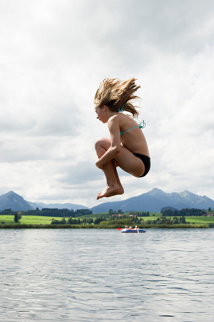 Teenage girl jumping into lake Hopfensee, Fuessen, Allgaeu, Bavaria, Germany