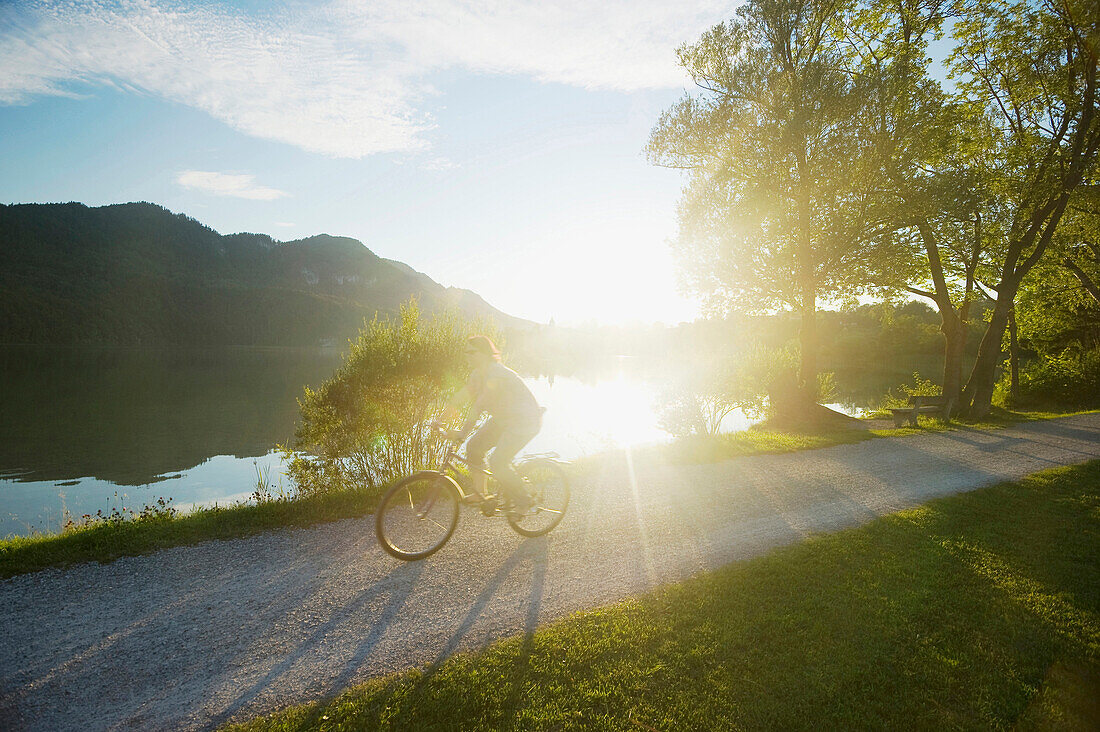 Woman cycling along lake Weissensee, Fuessen, Allgaeu, Bavaria, Germany