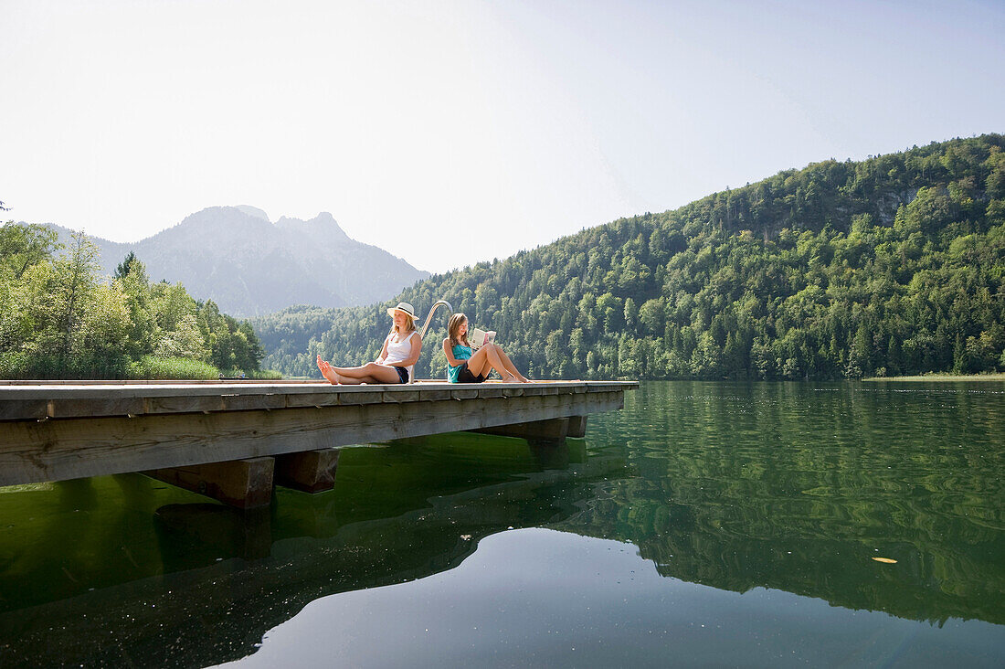 Two teenage girls sitting on a jetta at lake Schwansee, Schwangau, Allgaeu, Bavaria, Germany