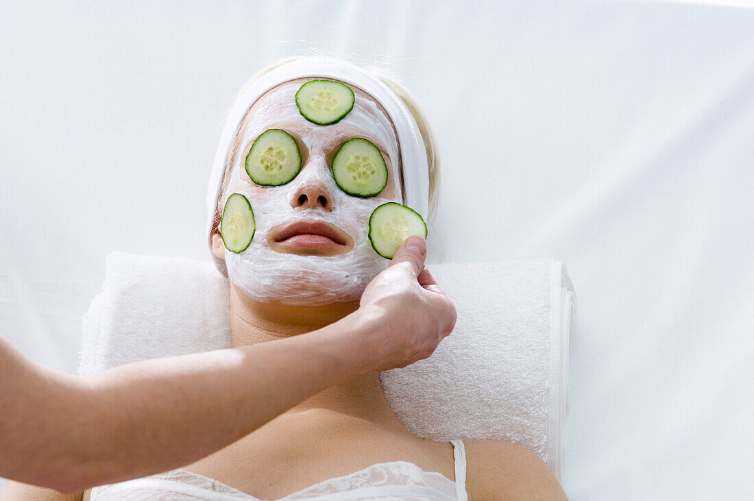 Portrait of a young woman with beauty mask on her face and slices cucumber on her eyes