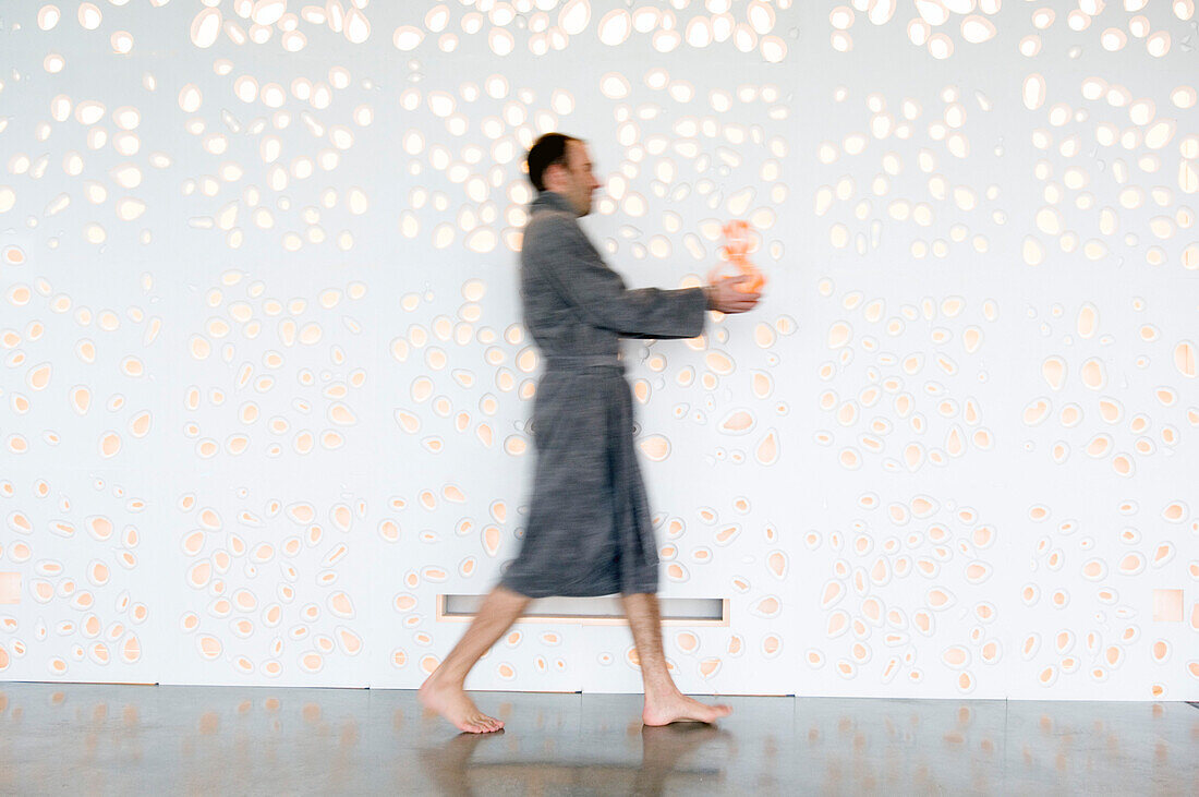 Man in grey bathrobe, walking, holding a vase, side view